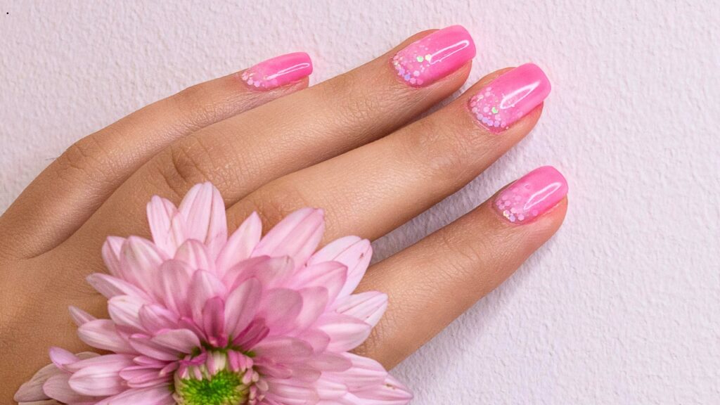 Elegant soft pink manicure with glitter nail art on healthy natural nails, symbolizing proper nail care and beauty.