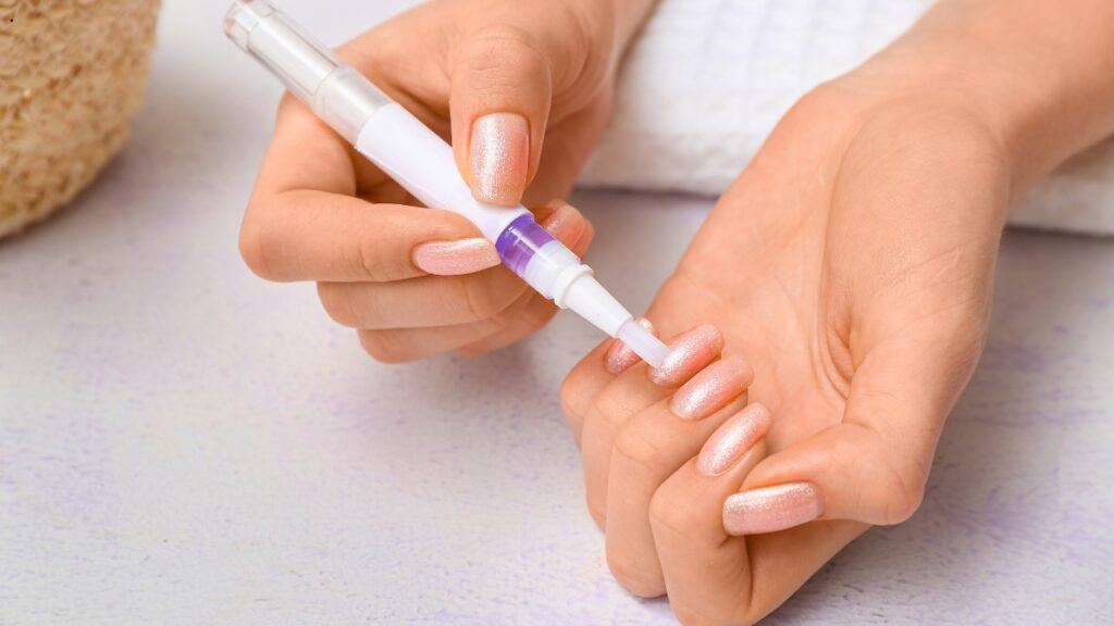 Applying cuticle oil to professional nail extensions as part of a daily aftercare routine to keep nails healthy and long-lasting.